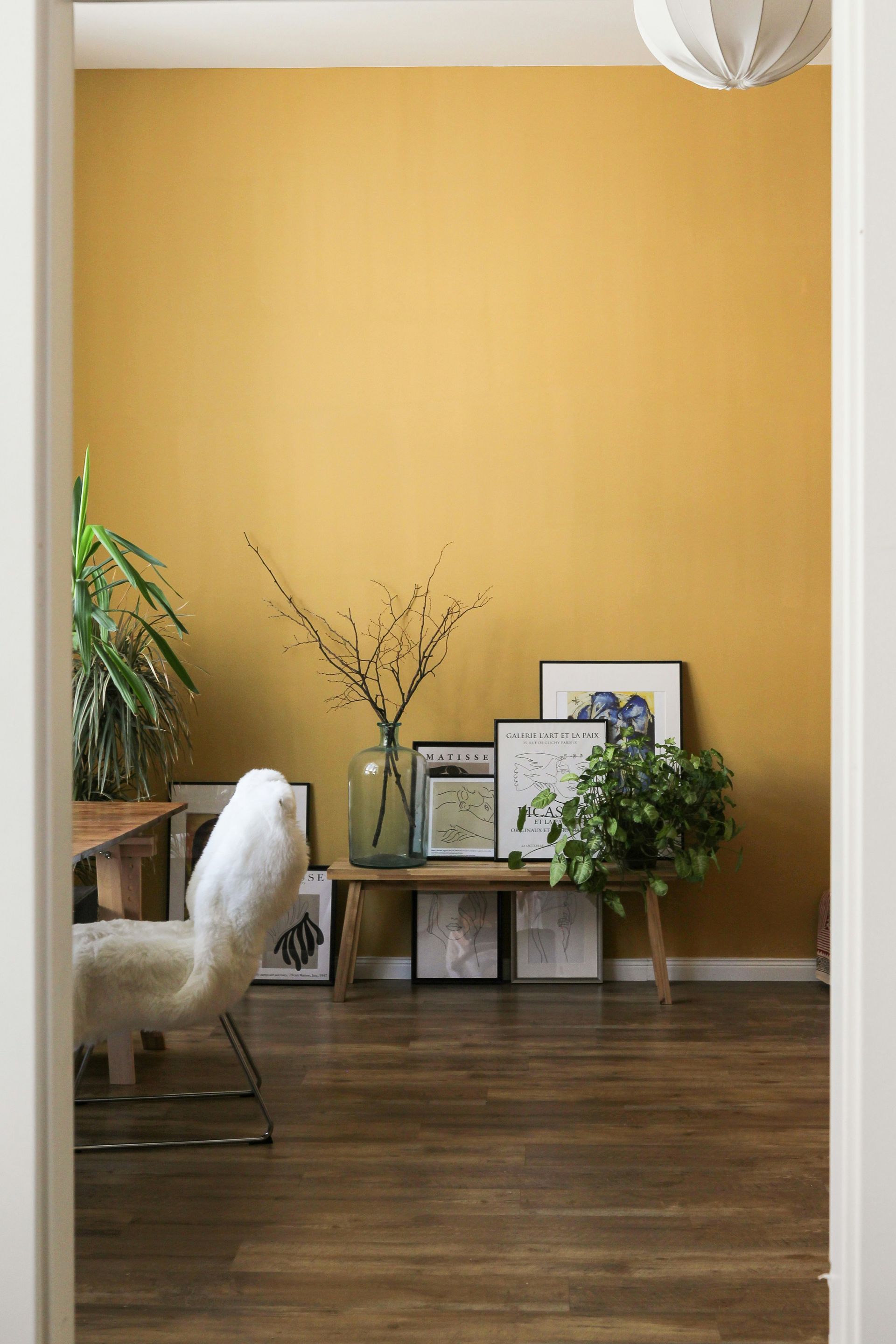 A wooden bench with framed art and plants against a mustard yellow wall
